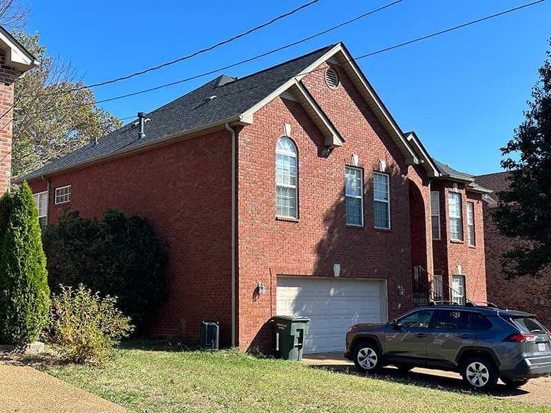 Red brick house with a garage, large windows, and green grass in front on a sunny day.