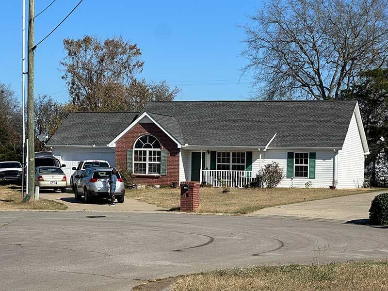 Single-story white house with brick accent, parked cars, and clear blue sky background.