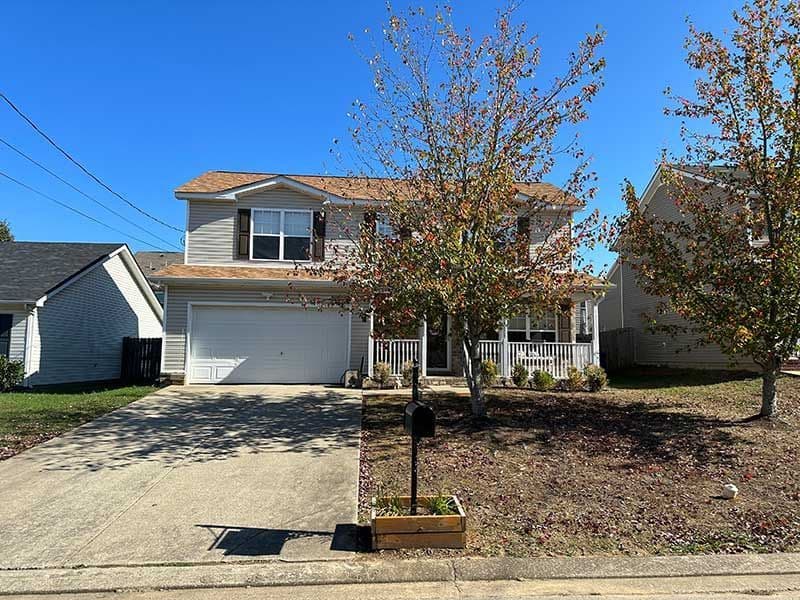 Two-story home with porch, garage, and autumn trees in a suburban neighborhood.