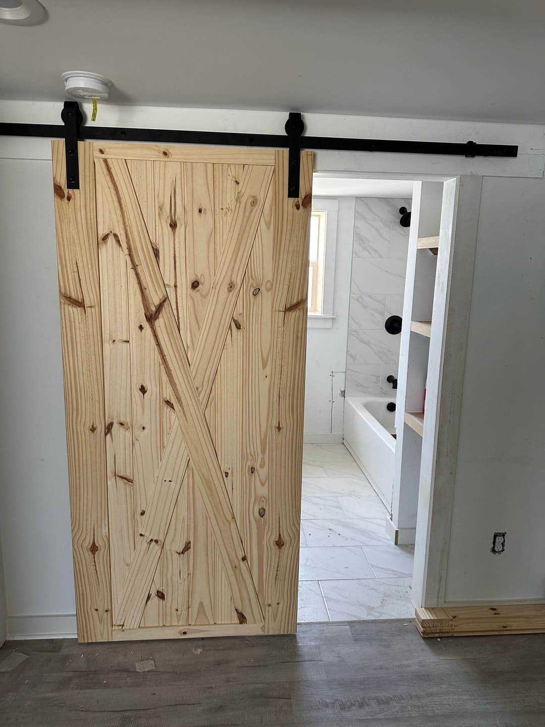 Sliding wooden barn door with diagonal paneling leading to a modern bathroom.
